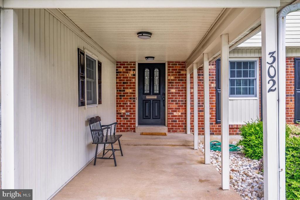 Covered porch with a black front door, brick walls, and a bench at 302.