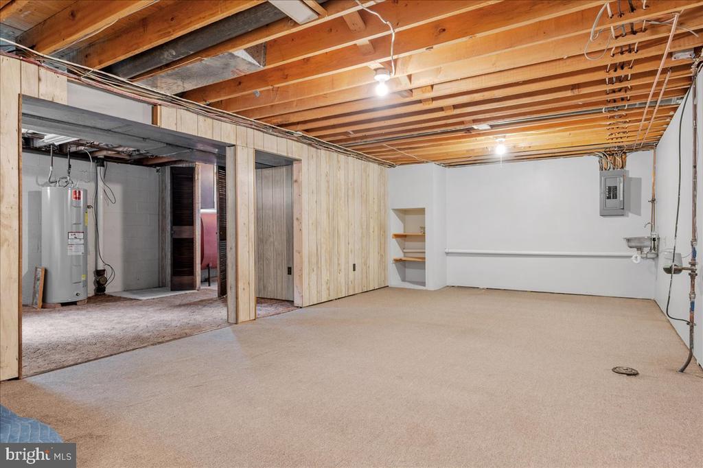 Unfurnished basement with exposed joists, carpeted floor, and a water heater.