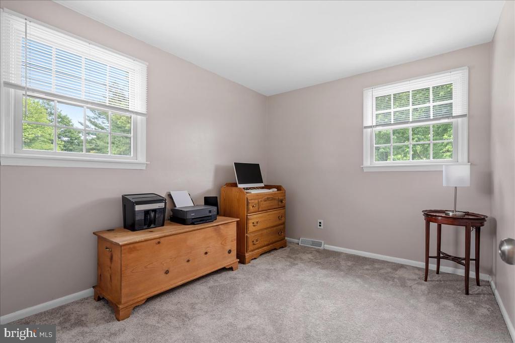 Furnished home office with wooden dressers, computer equipment, gray carpet, and two windows.