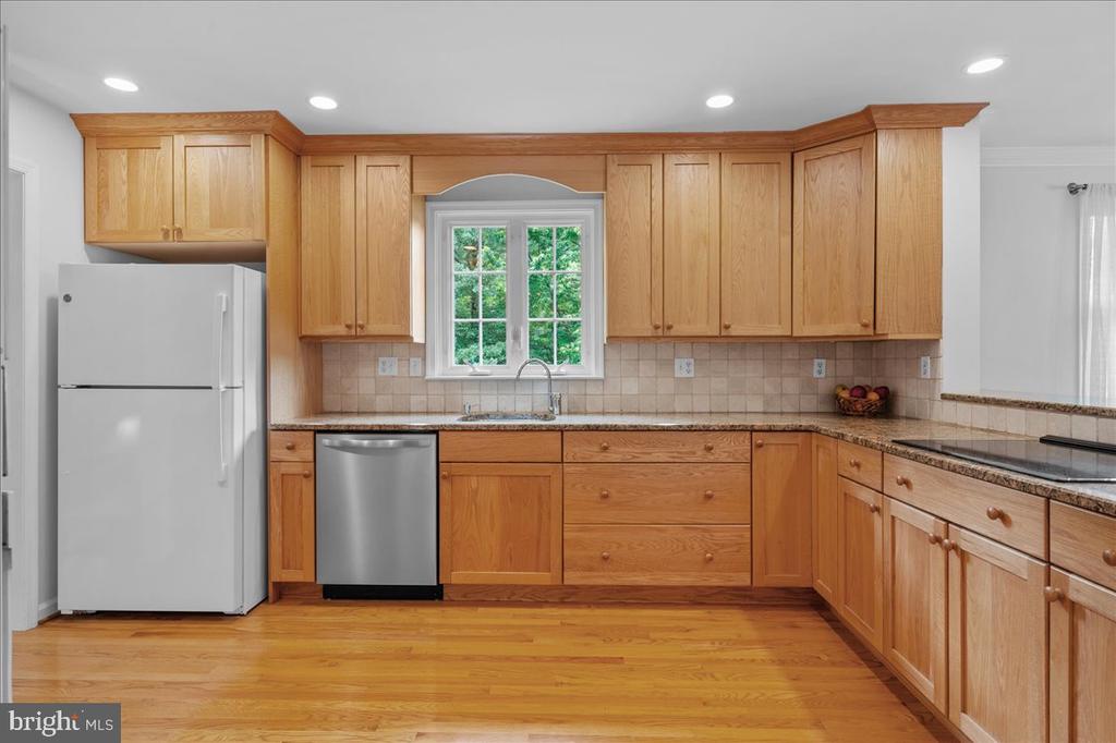 Kitchen with honey-colored cabinets, granite counters, hardwood floors, and a window above the sink.