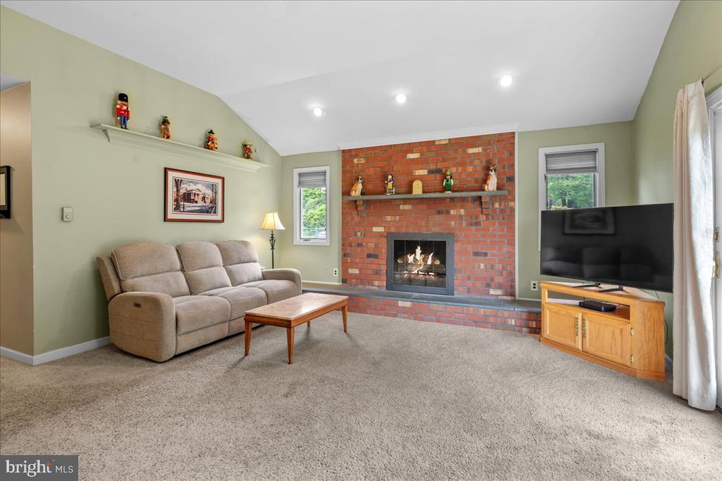 Living room with a brick fireplace, vaulted ceiling, beige carpet, and sofa.