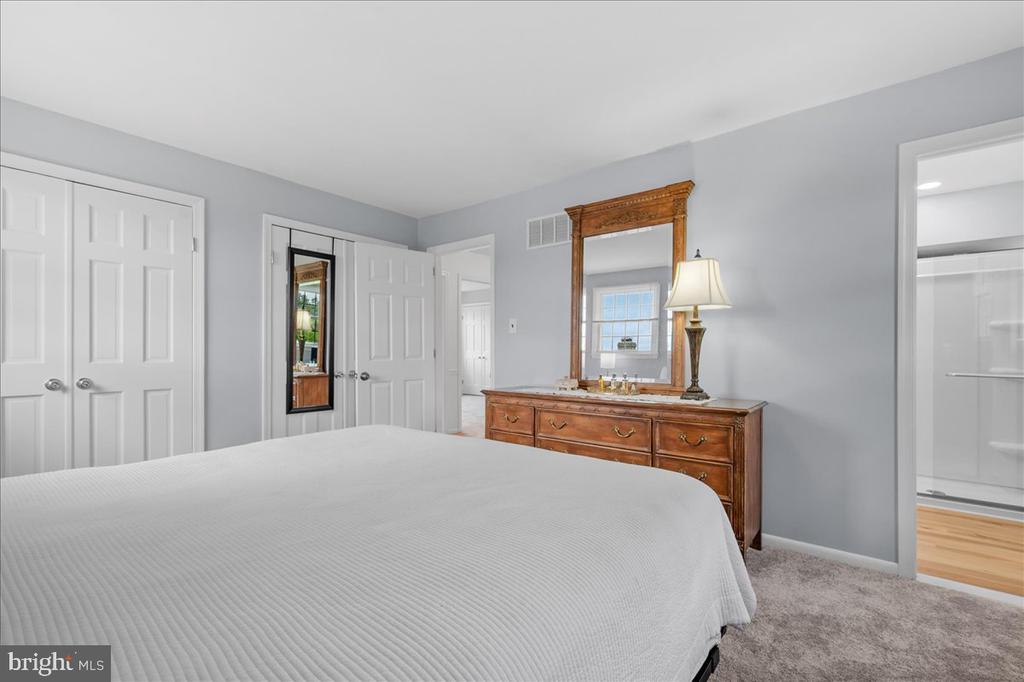 Bedroom with a white-covered bed, wooden dresser and mirror, and adjoining bathroom.