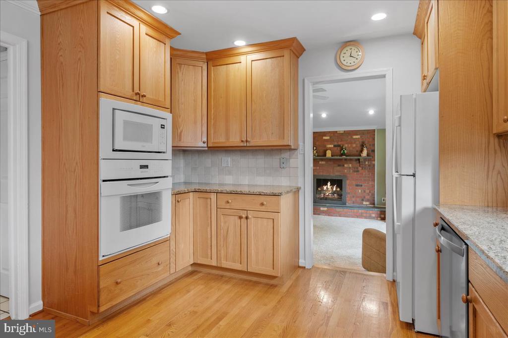 Kitchen with honey-colored cabinets, granite counters, double wall oven, and hardwood floors.