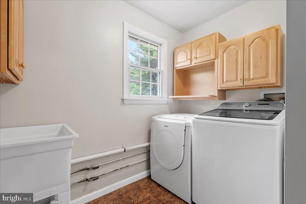 Laundry room with a washer and dryer, light wood cabinets, a utility sink, and a window.