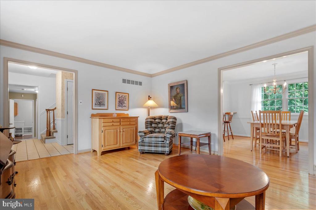 Living room with hardwood floors and plaid armchair, opening to a dining room with large windows.