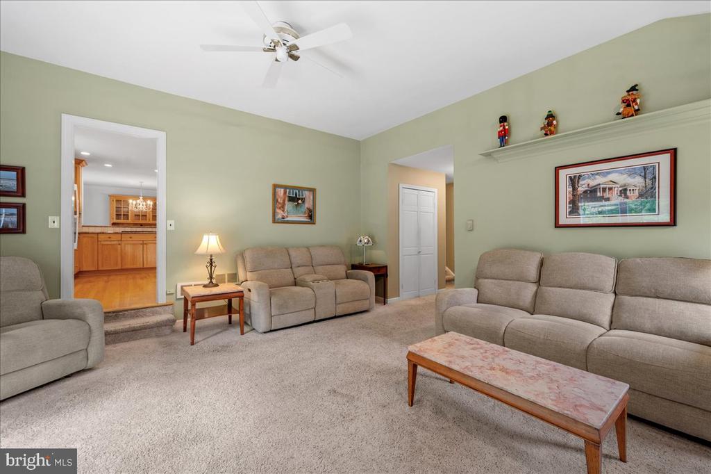 Living room with green walls, beige reclining sofas, and an open view into the wood-cabinet kitchen.