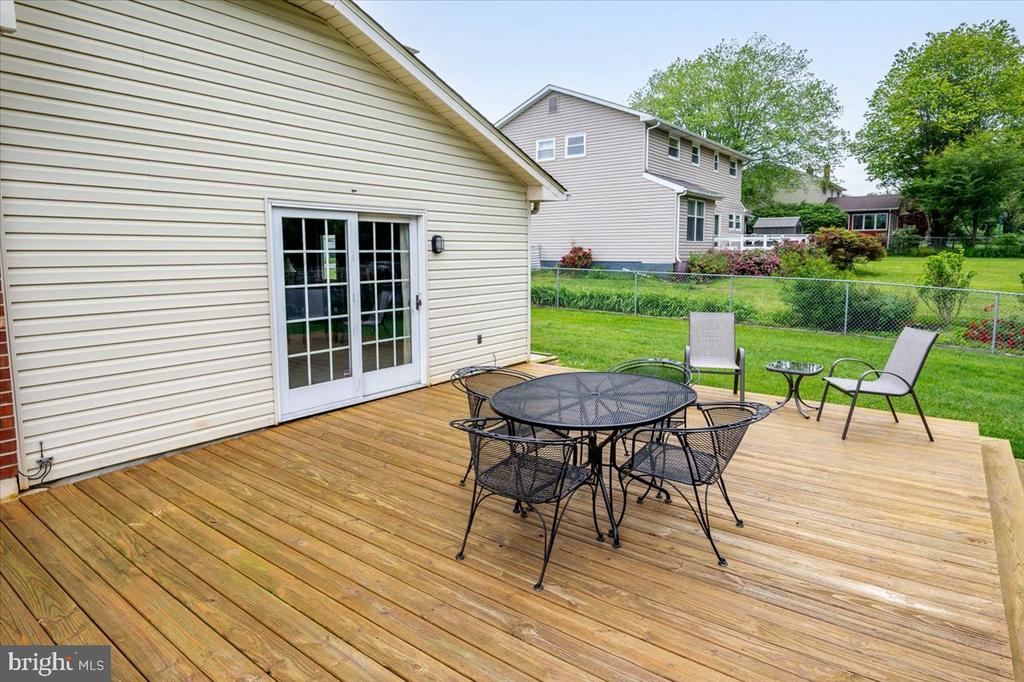 Backyard deck with a black metal dining set, lounge chairs, and lawn beyond a chain-link fence.