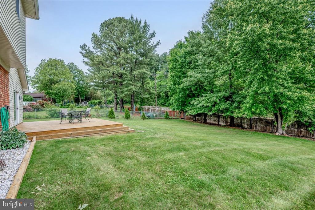 Spacious fenced backyard with a raised wooden deck, patio furniture, lawn, and mature trees.