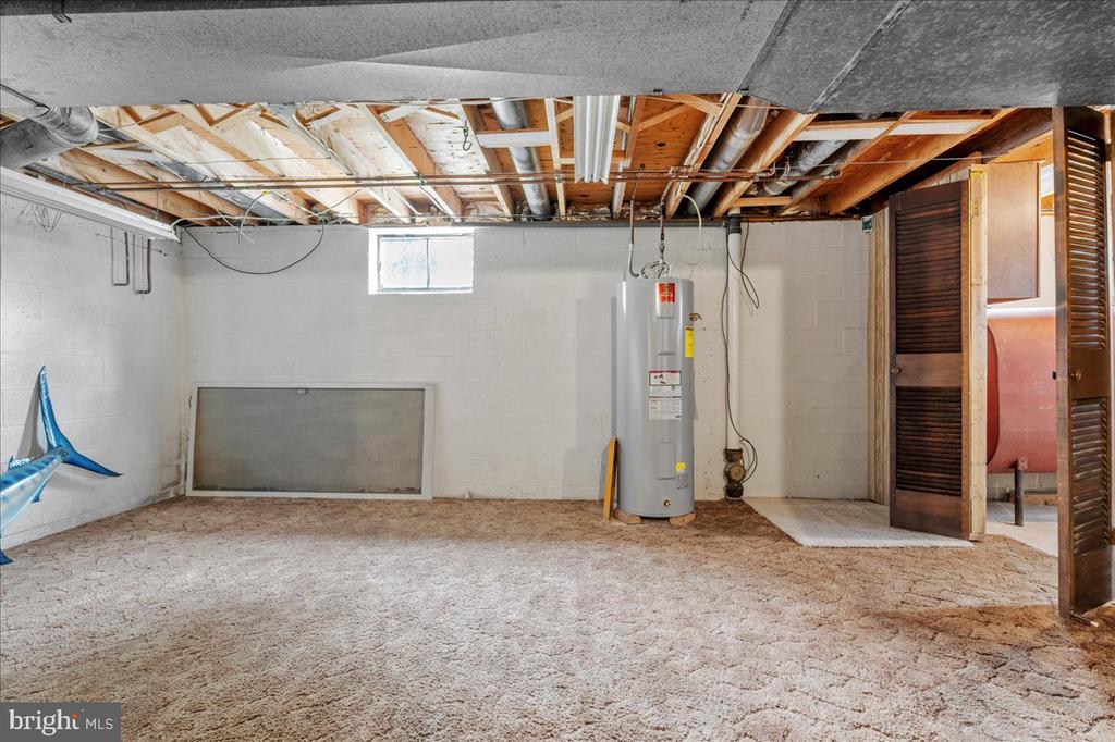 Unfinished basement with carpet, exposed ceiling joists, and a water heater.