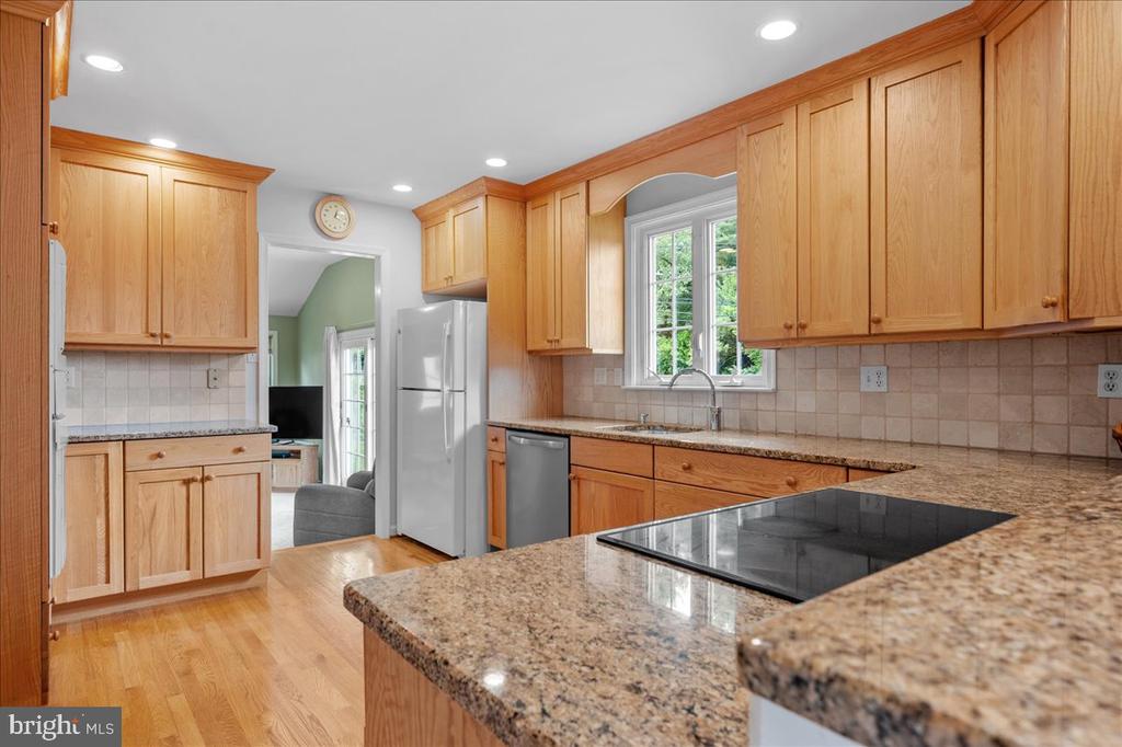 Kitchen with wood cabinets, granite counters, and a cooktop peninsula beside a window.
