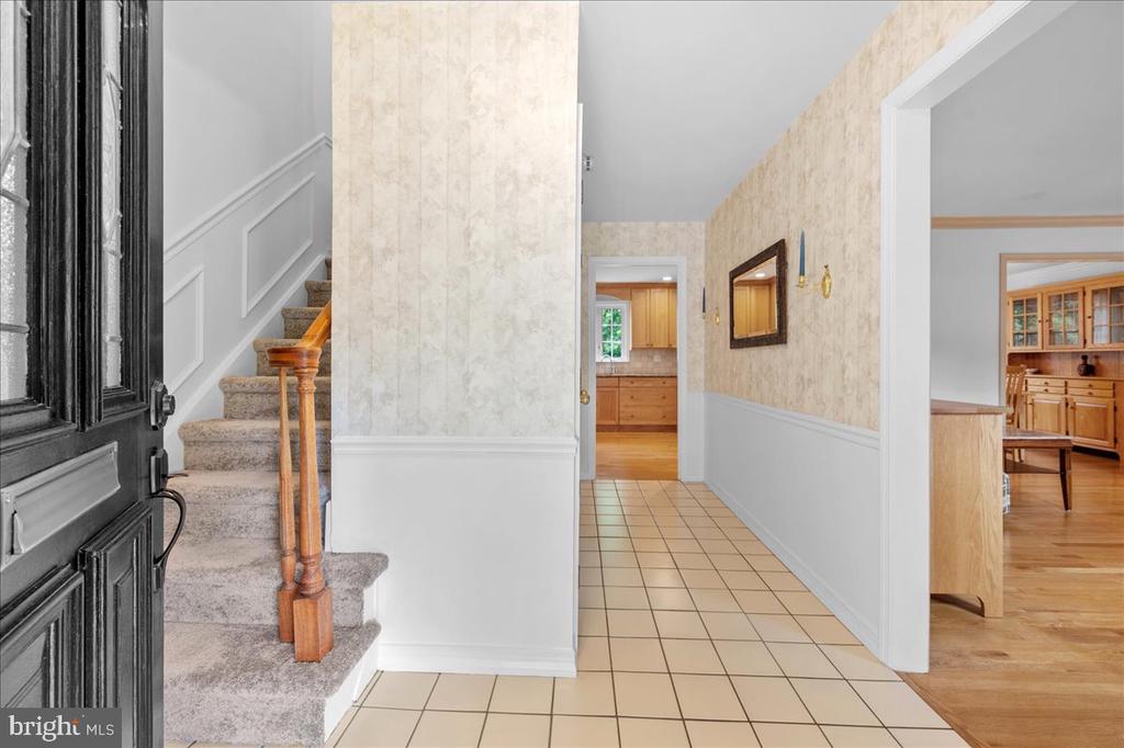 Entry hall with tiled flooring, a carpeted staircase, and doorways leading to the kitchen and adjoining room.