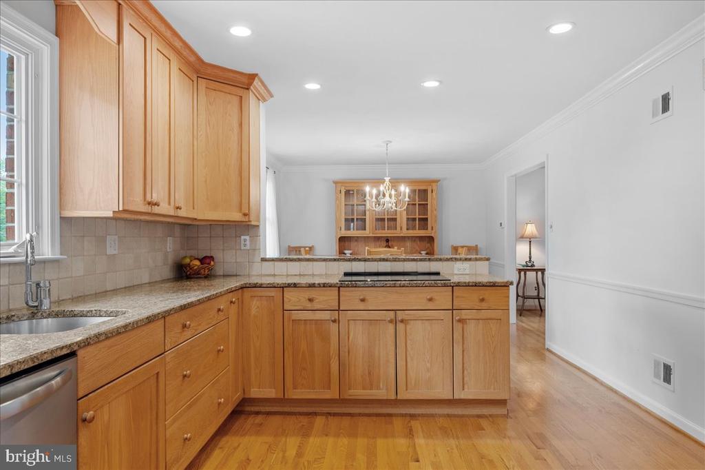 Kitchen with honey-colored wood cabinetry, granite counters, and a central island cooktop.