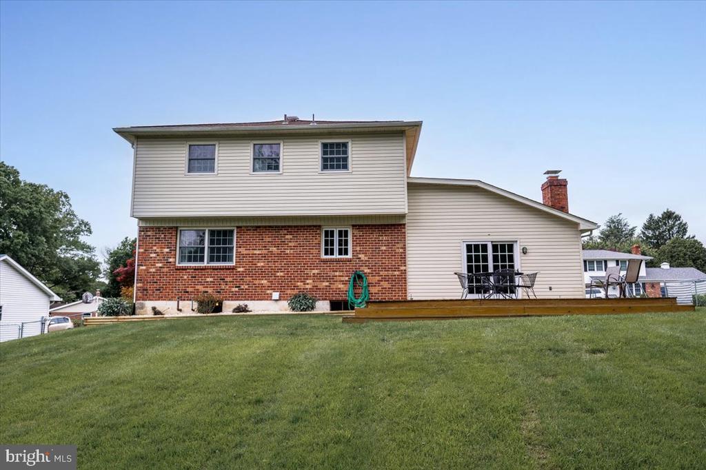 Rear exterior of a two-story brick and beige-sided house with a raised deck and sloping lawn.