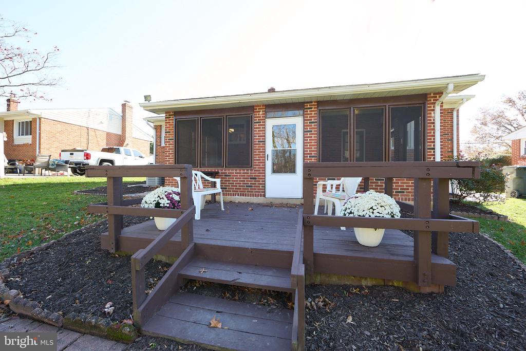 Brick home with a raised wooden deck, white chairs, and potted flowers.