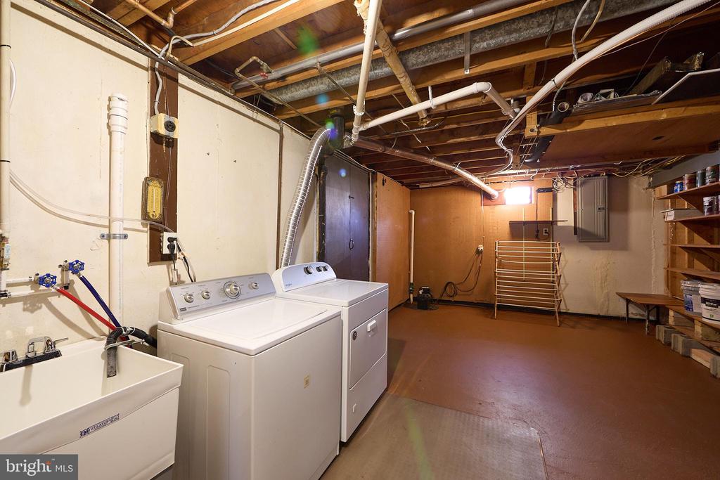 Basement laundry area with washer, dryer, utility sink, and exposed ceiling joists.