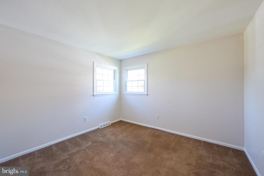 Vacant bedroom with brown carpet and two adjoining windows.