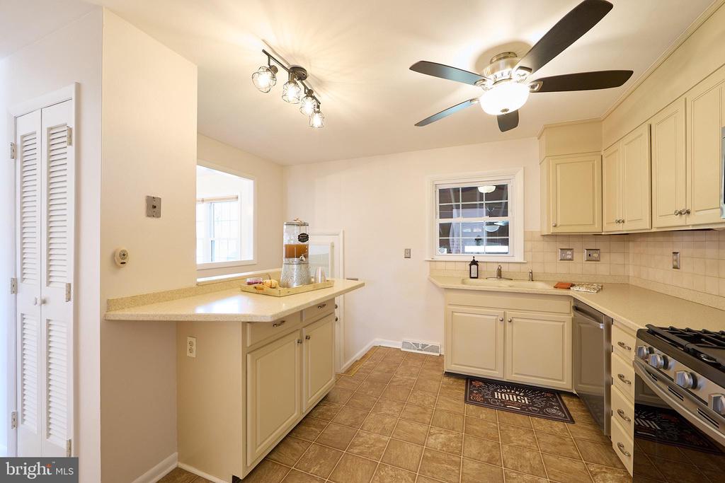 Kitchen with cream cabinets, a peninsula, brown tile flooring, and a ceiling fan.