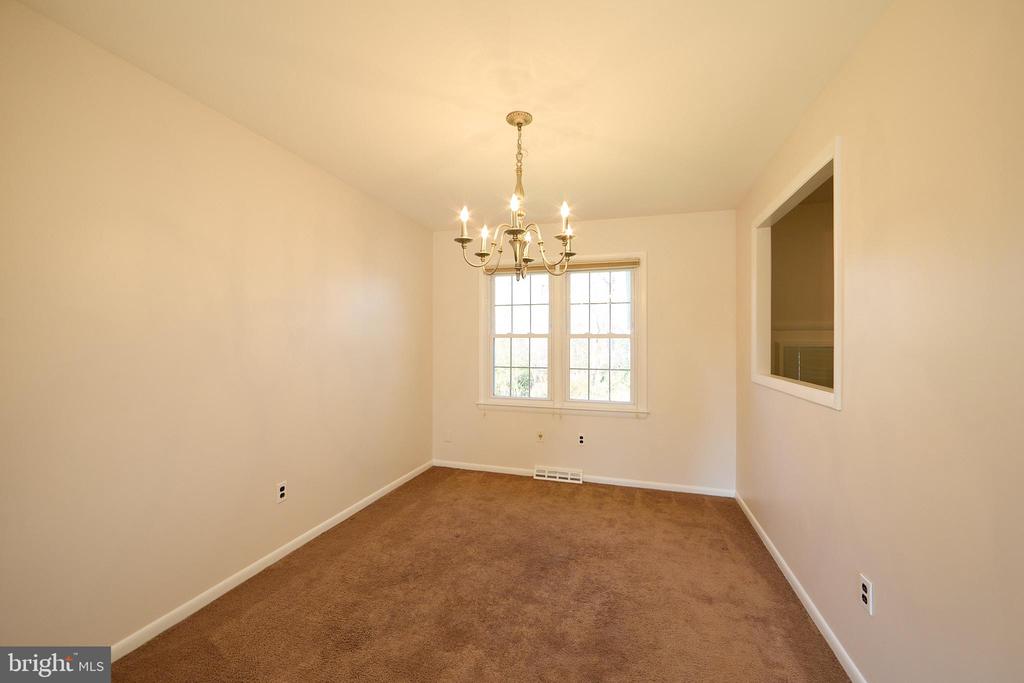 Empty carpeted room with a brass chandelier, double window, and pass-through opening.