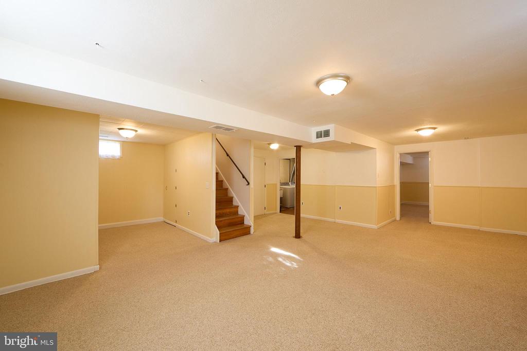 Finished basement rec room with beige carpeting, a staircase, and an open doorway.