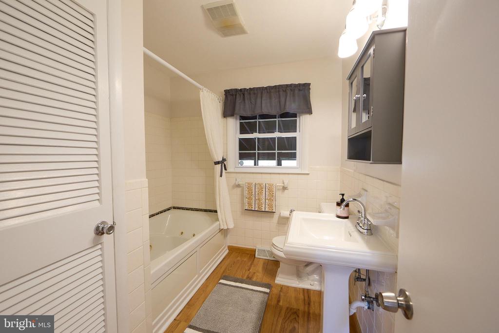Bathroom with a built-in tub, pedestal sink, and wood-look flooring.