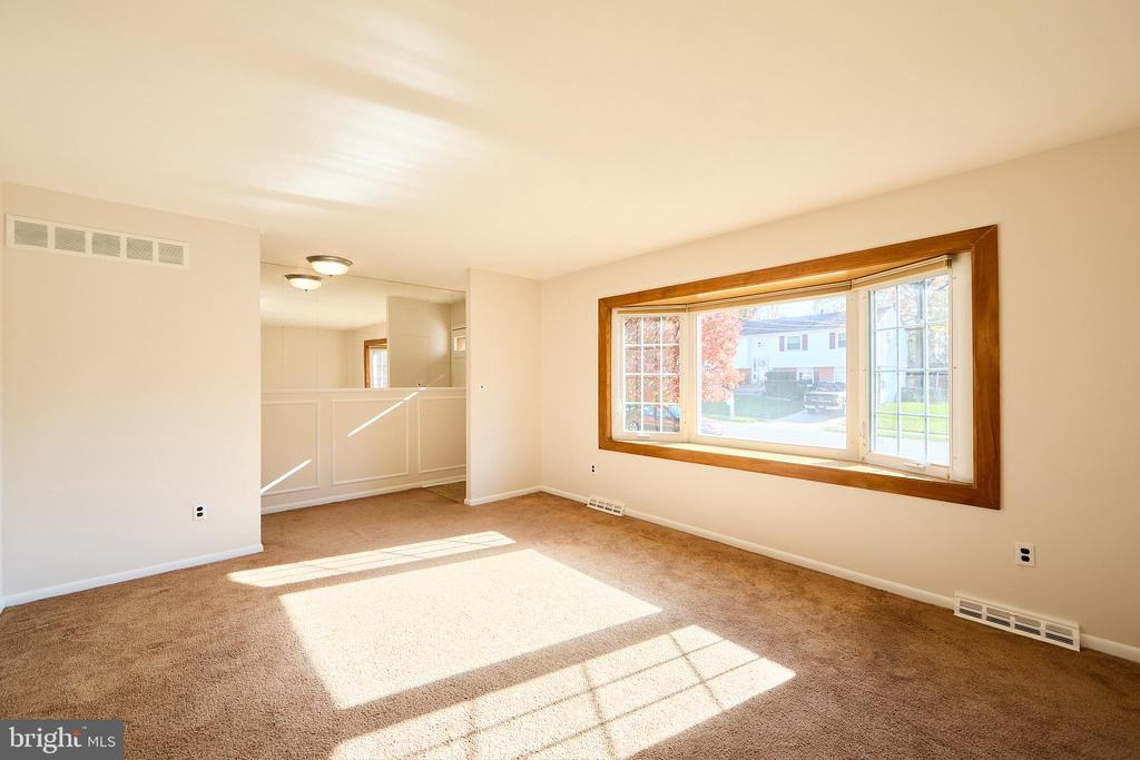 Empty living room with a large wood-trimmed picture window and sunlight across the carpet.