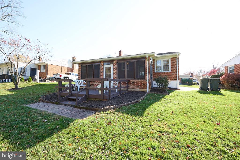 Rear of a brick home with a raised deck, screened porch, and broad lawn.