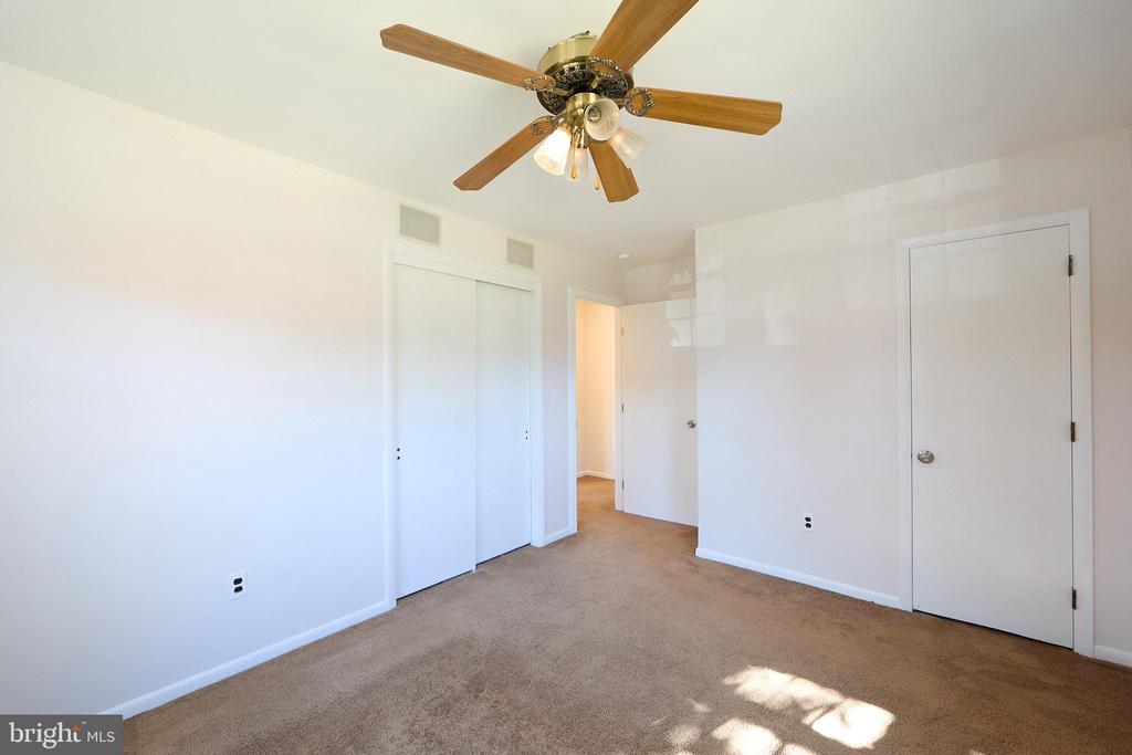 Empty bedroom with beige carpet, a wood-tone ceiling fan, and a sliding-door closet.