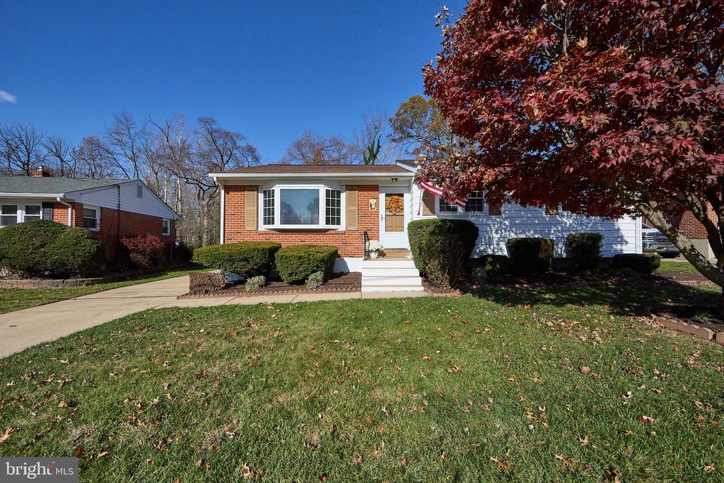 Single-story brick-and-siding home with a bay window, front lawn, and large red-leaved tree.
