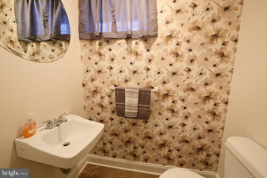 Bathroom with beige floral wallpaper, a pedestal sink, and a curtained window.