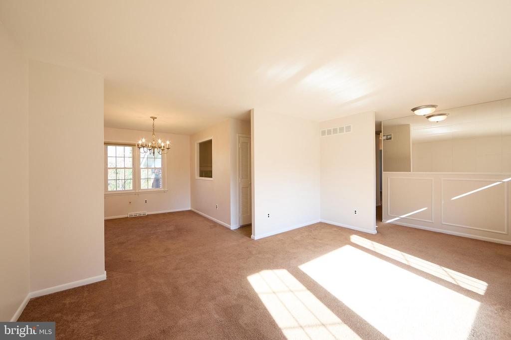 Empty carpeted room with a chandelier by the window and sunlight across the floor.