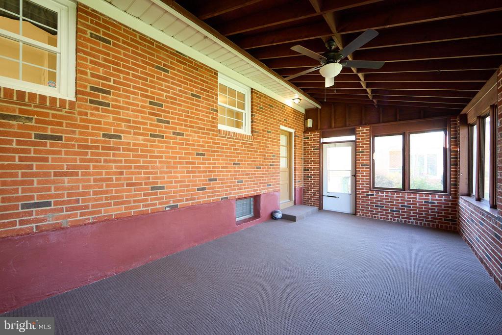 Empty brick sunroom with carpet, exposed wood ceiling beams, a ceiling fan and multiple windows.