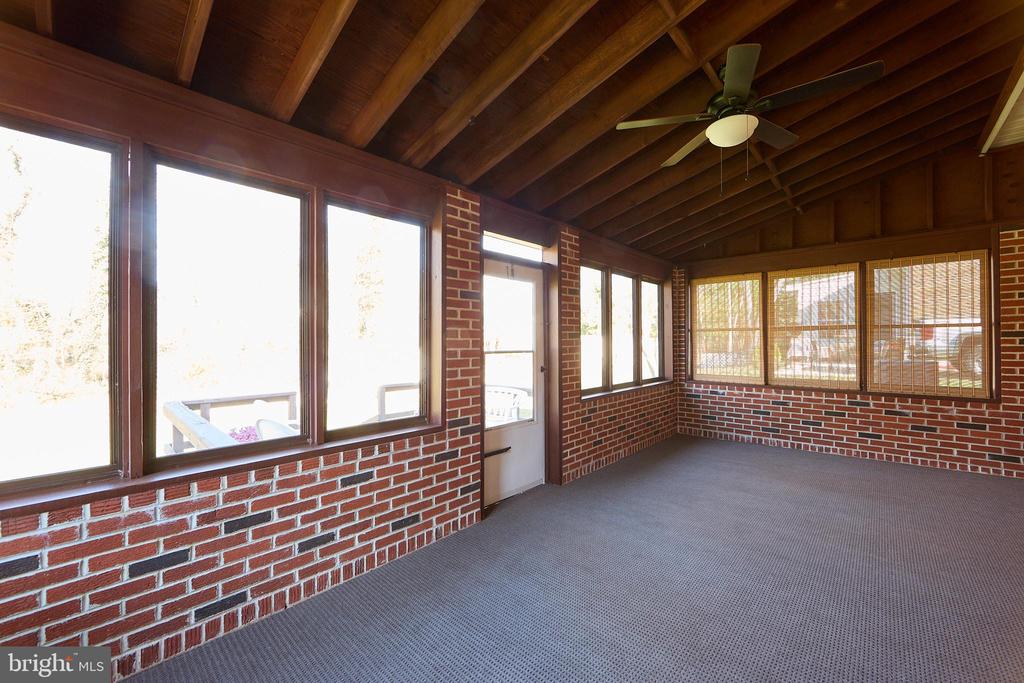 Empty sunroom with brick walls, large windows, gray carpet, and an exposed wood-beam ceiling.