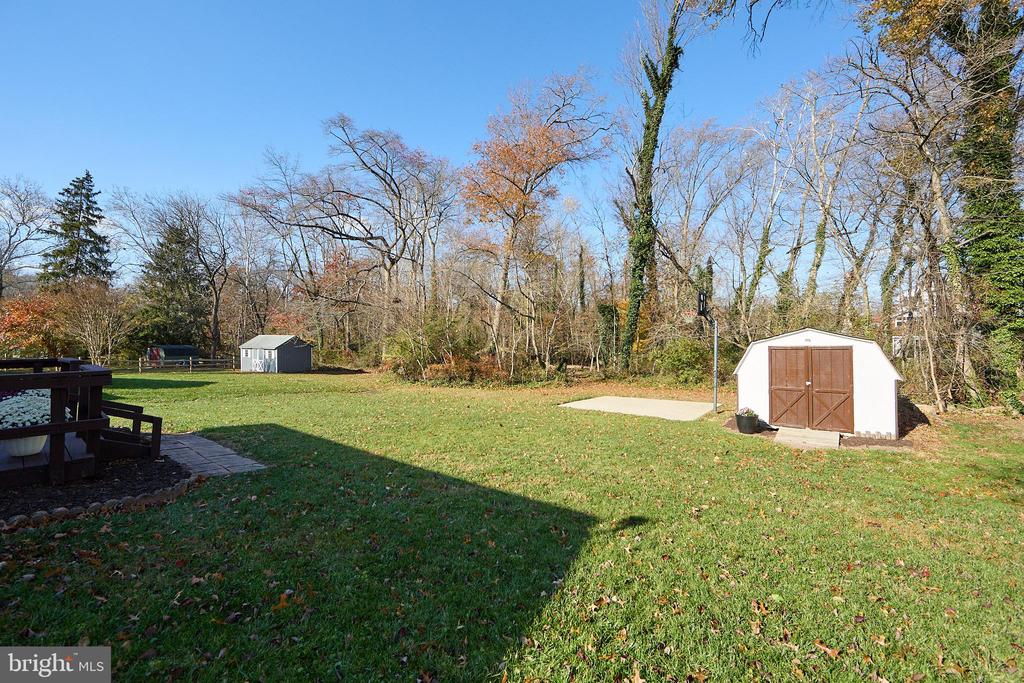 Backyard with a broad lawn, two sheds, a raised deck, and trees.