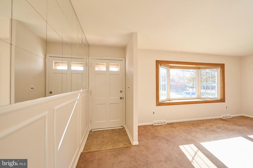 Vacant entry and living area with mirrored wall, tiled floor, and large bay window.