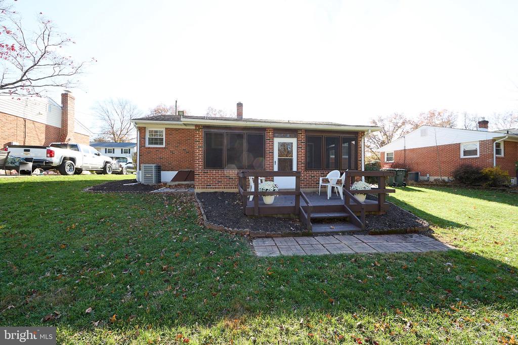 Rear of a brick ranch home with a raised wooden deck, screened windows, and a broad lawn.