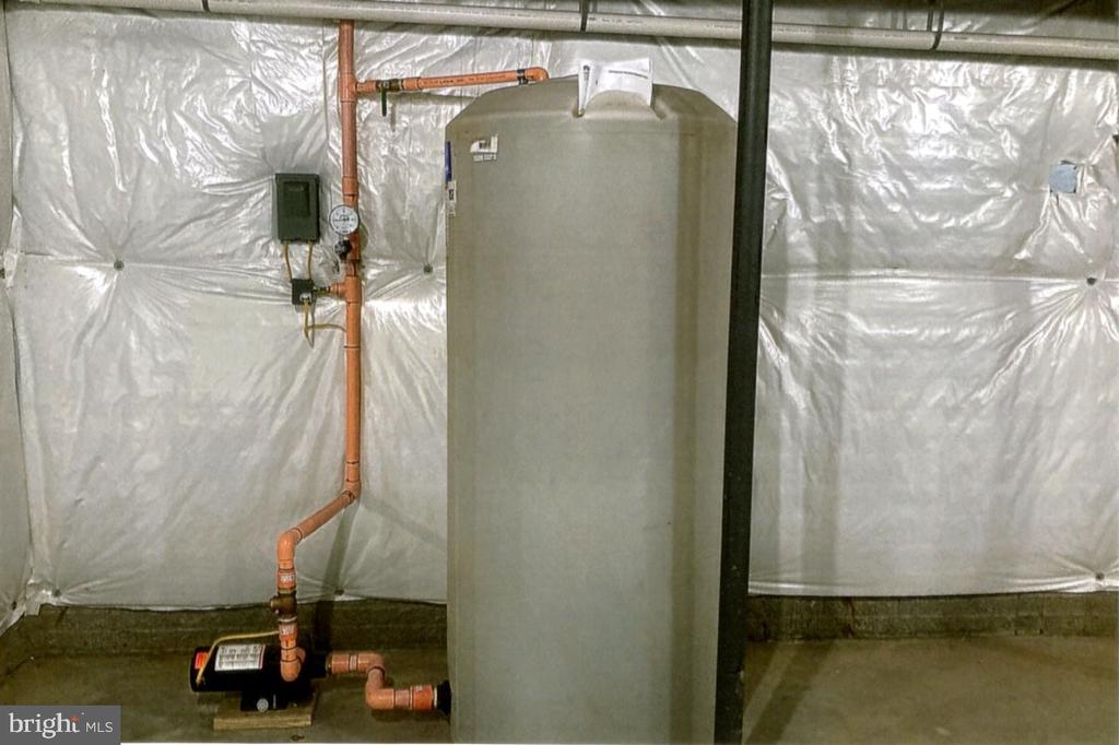 Basement utility area with a large water tank, exposed pipes, and a pump.