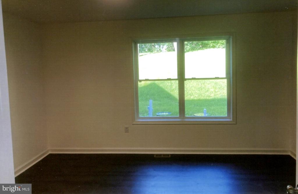 Empty room with dark hardwood floors and a double window overlooking a lawn.