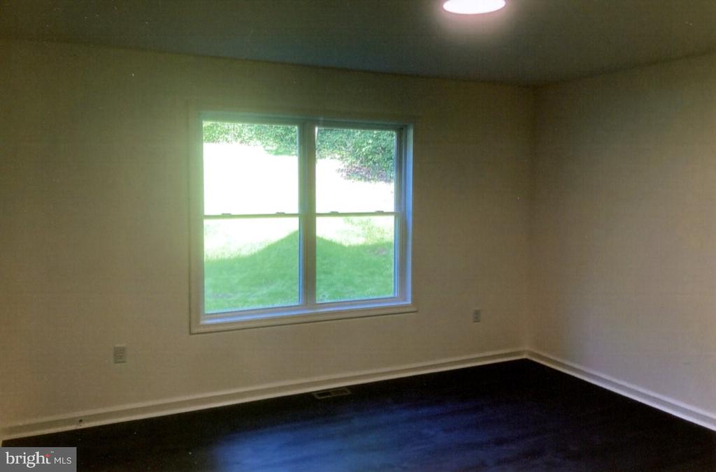 Empty room with dark flooring and a double window overlooking a green lawn.