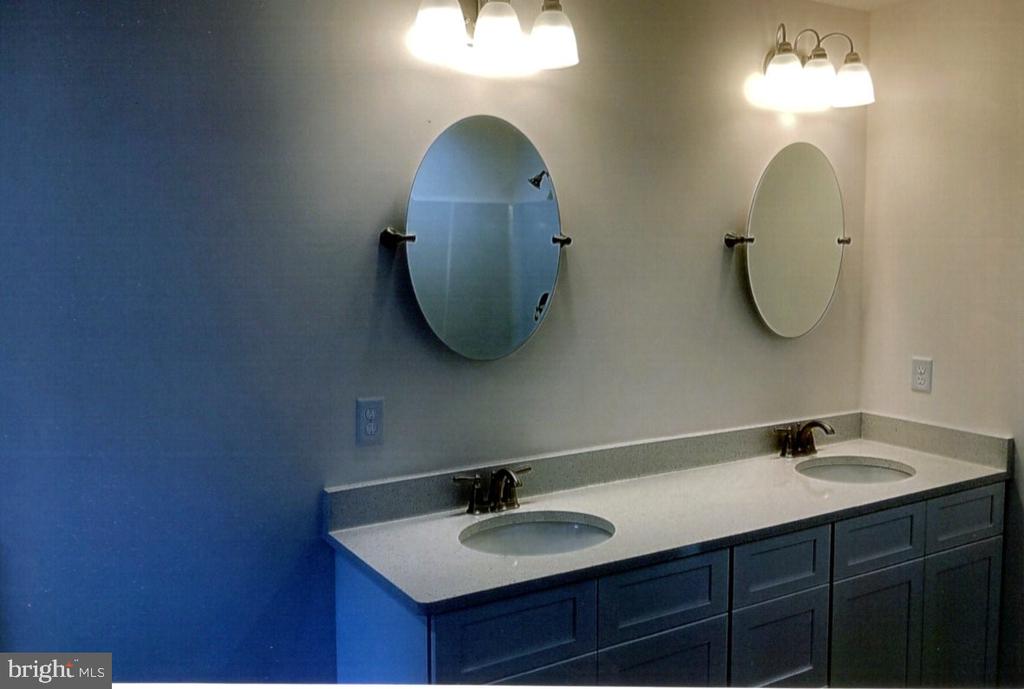 Bathroom double vanity with dark cabinets, pale countertop, and two oval mirrors.