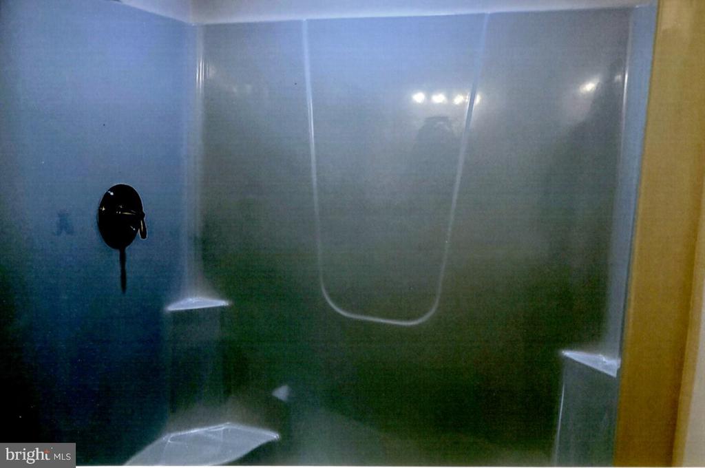 Bathroom shower with a glass enclosure, dark fixtures, and built-in corner shelves.