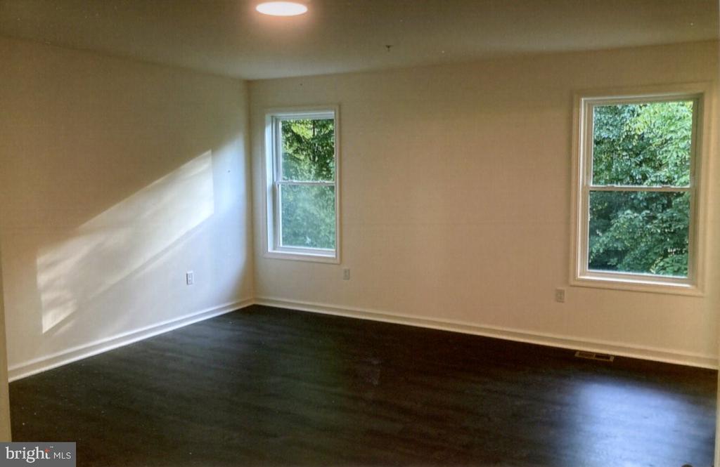 Empty room with dark hardwood floors, two windows, and sunlight across the wall.