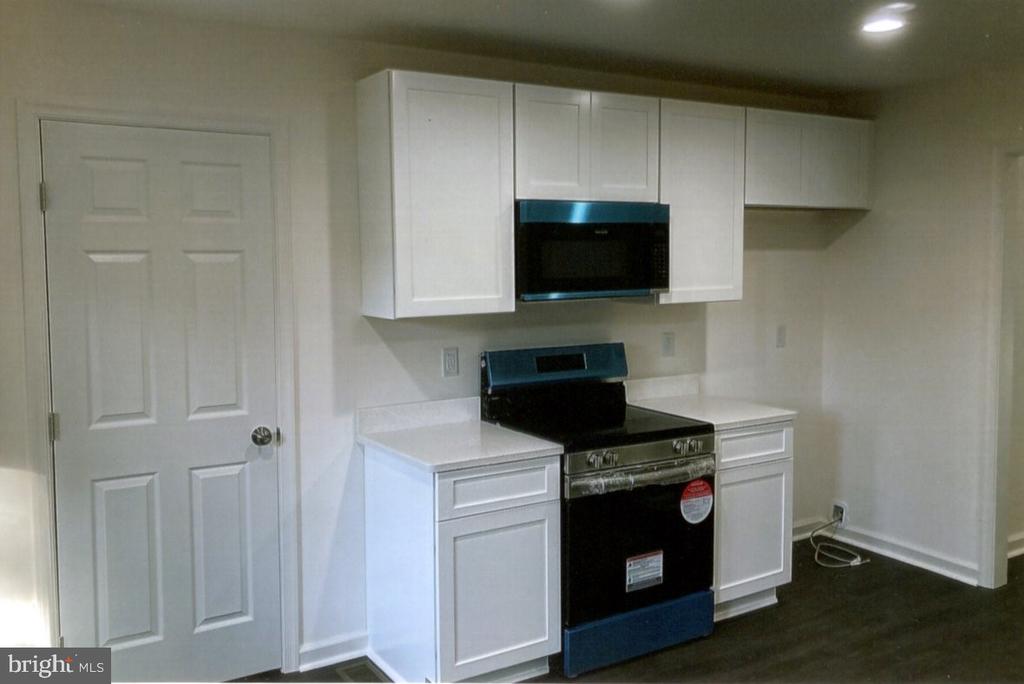 Kitchen with white cabinets, built-in microwave, black range, and dark flooring.