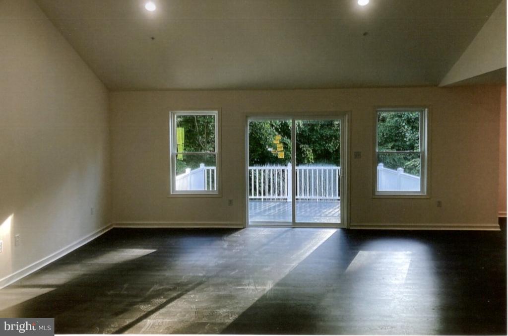 Empty living room with dark flooring and sliding glass doors opening onto a white-railed deck.