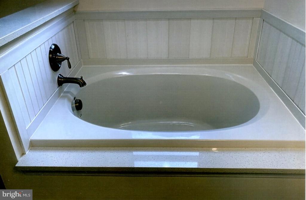 Built-in bathtub with dark fixtures and a white paneled surround.