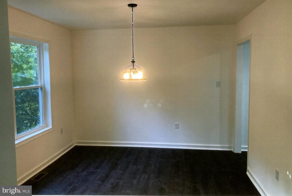 Empty dining room with dark flooring, a hanging light, and a window overlooking greenery.