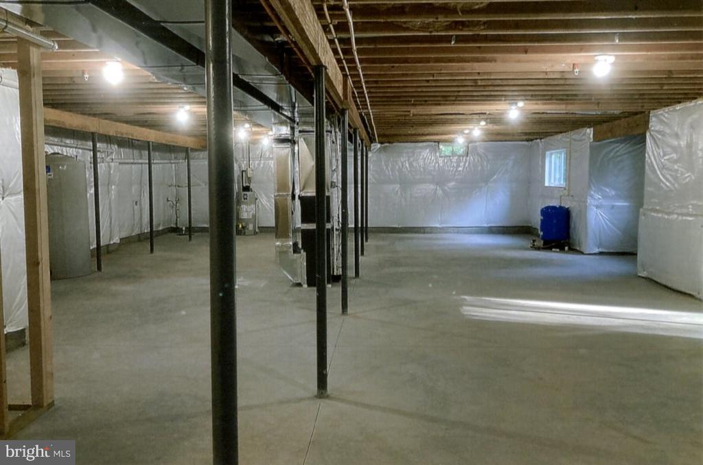 Unfinished basement with exposed joists, concrete floor, support posts, and plastic-covered walls.