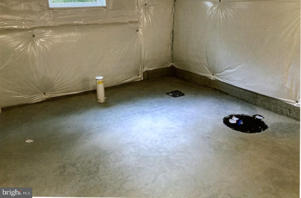 Unfinished basement with a concrete floor, plastic-covered walls, and floor openings.