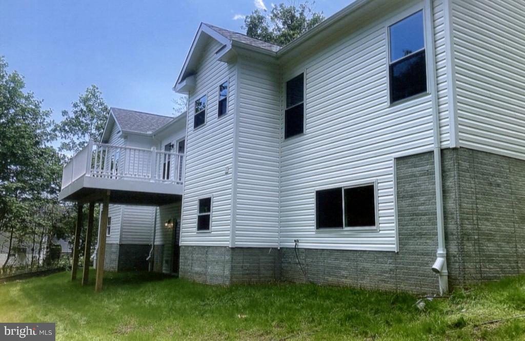 Two-story white-sided house with a raised deck overlooking a grassy yard.