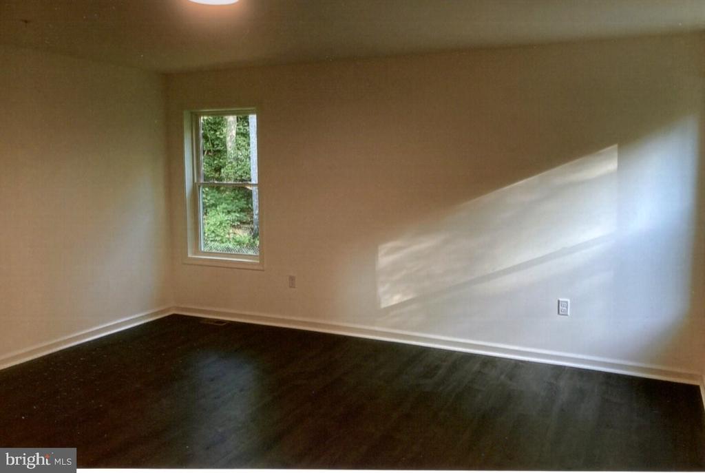 Vacant room with dark flooring, white trim, and a window overlooking trees.