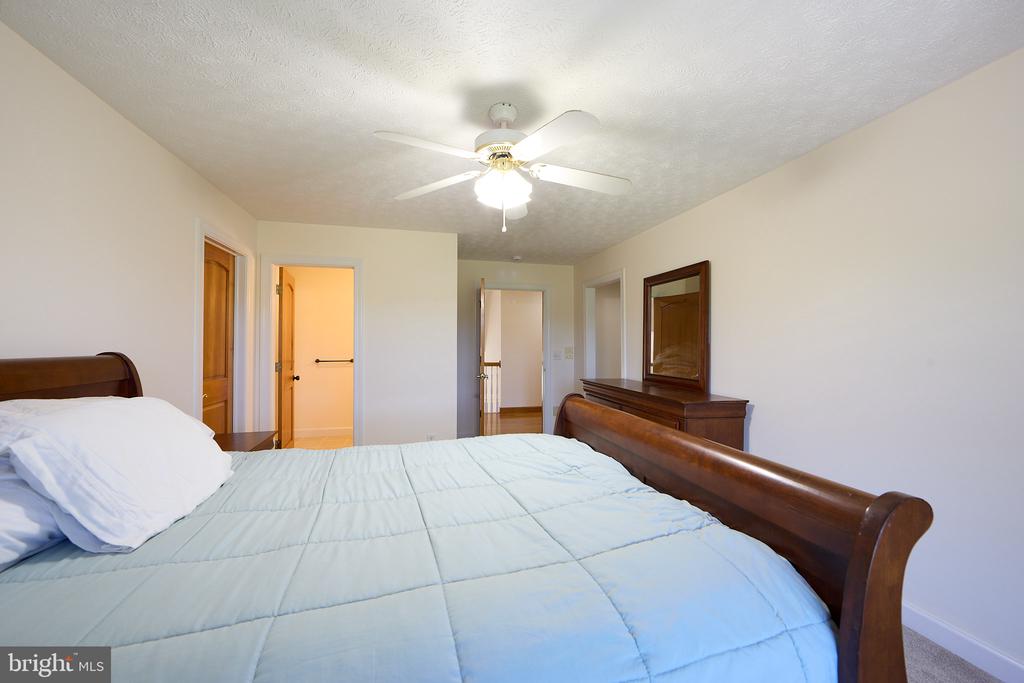 Bedroom with a wooden bed, pale blue quilt, ceiling fan, and dresser with mirror.